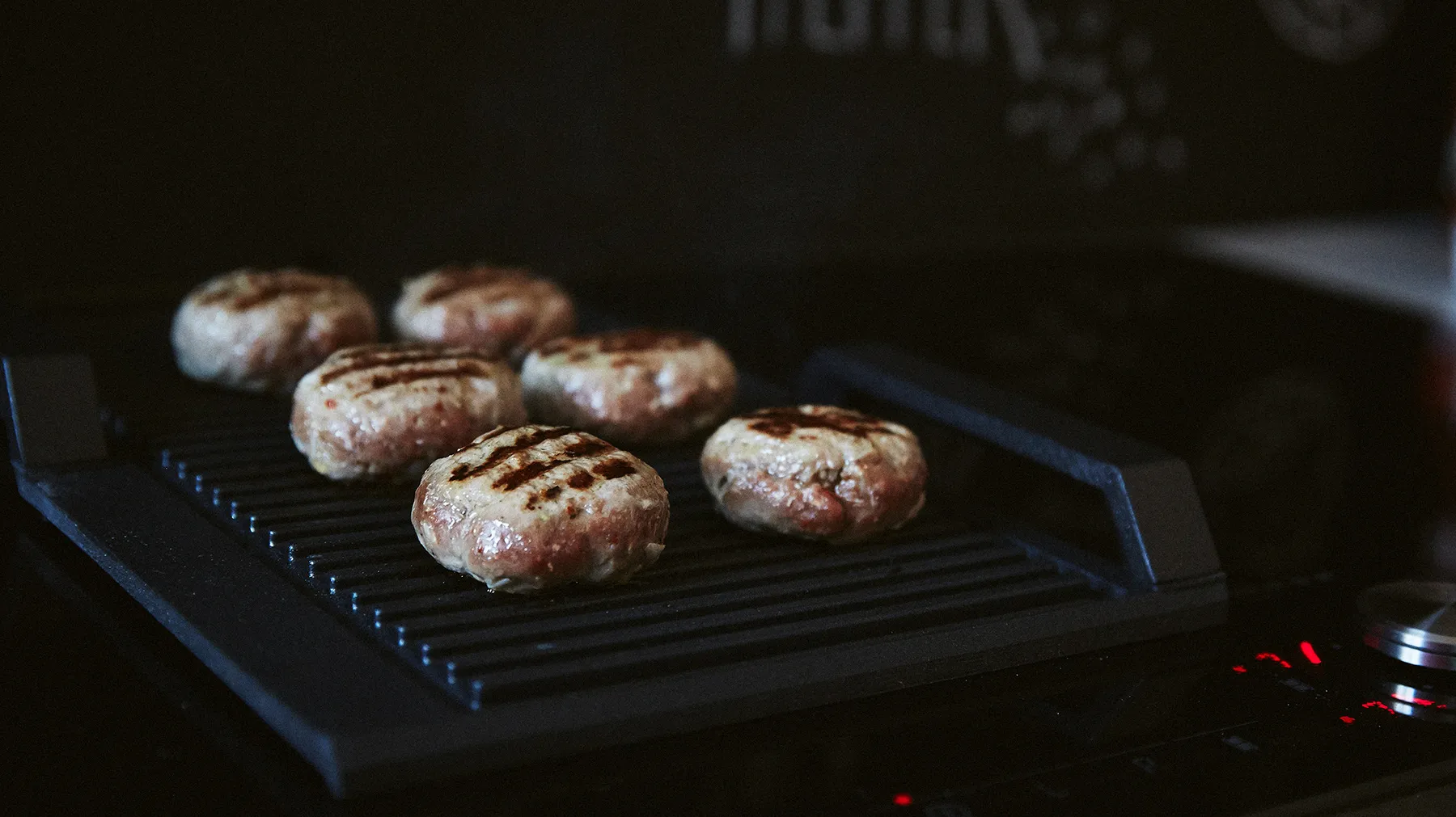 Hamburger alla griglia su una grigliata nera, con uno sfondo scuro.