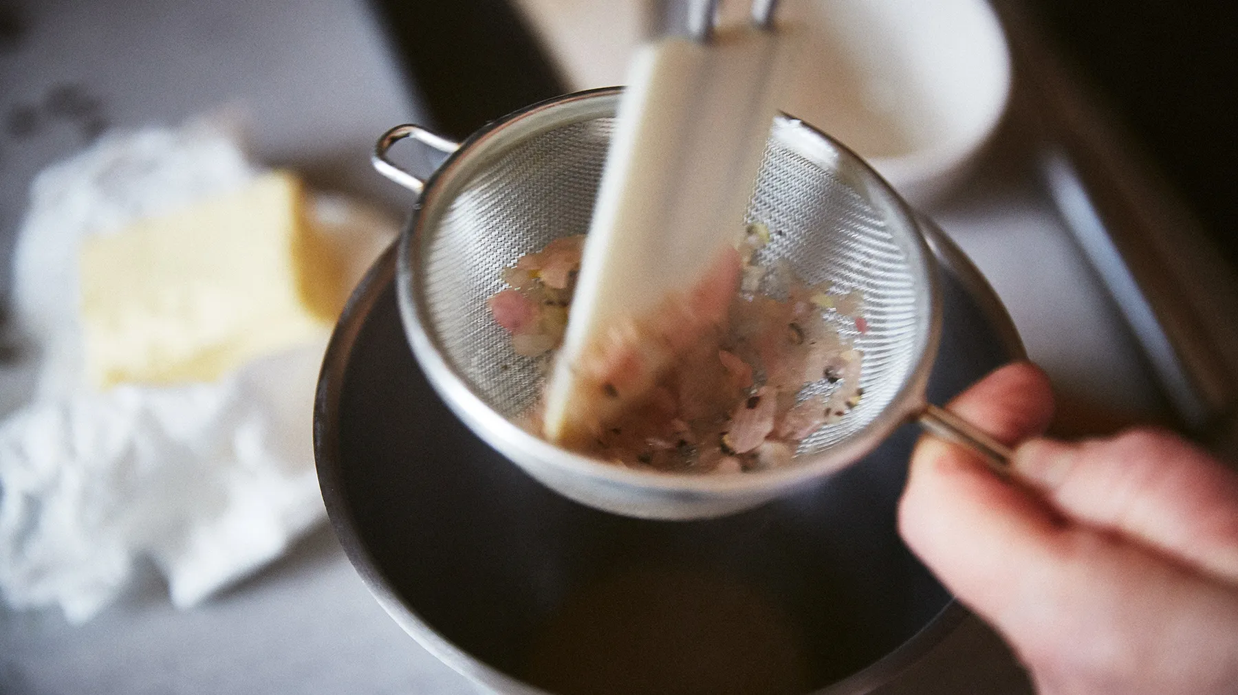 Strainer con foglie di tè, mano che tiene un cucchiaio, sfondo sfocato.