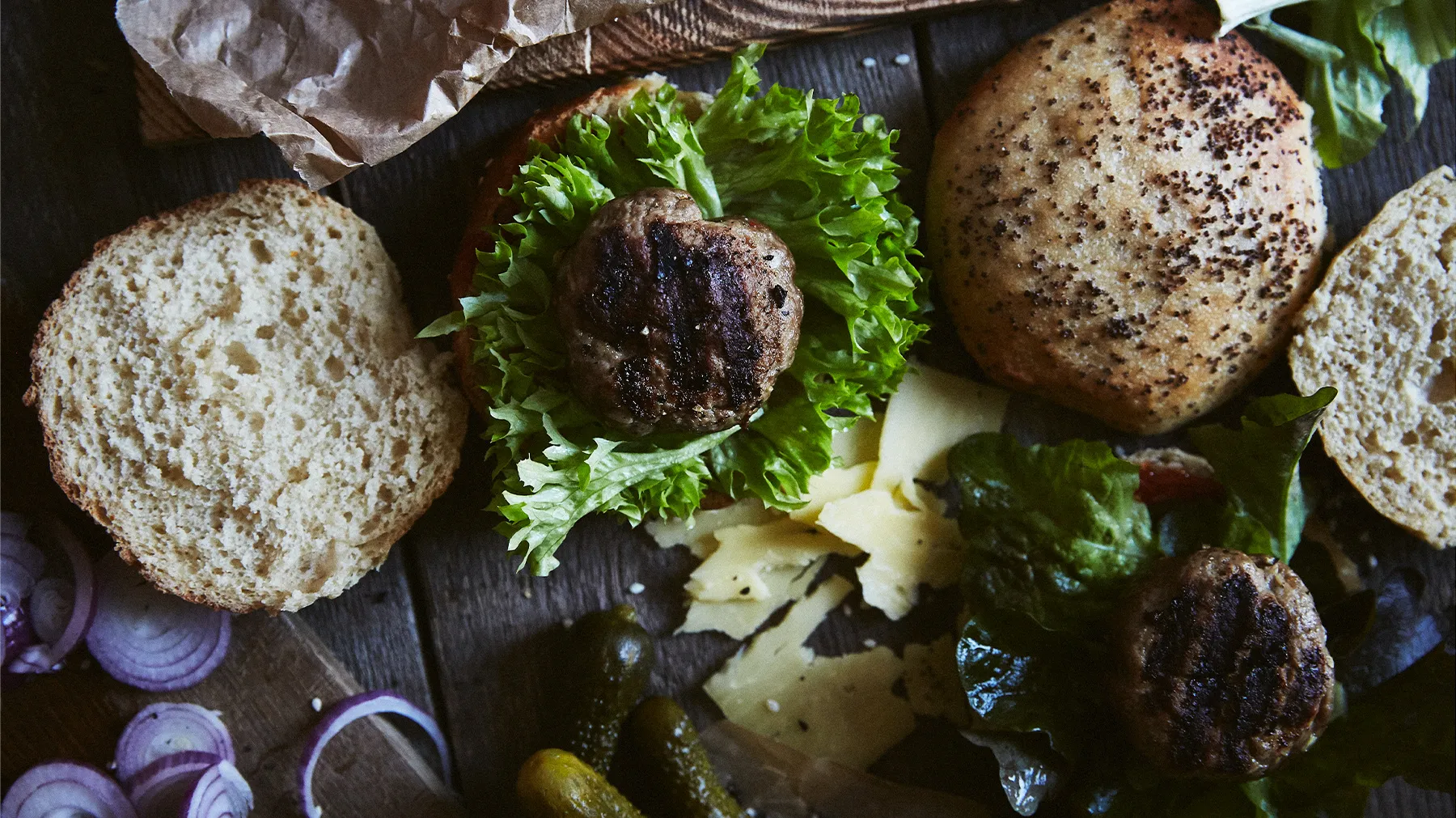 Panini Hamburger, lattuga, tortini alla griglia, cipolle e cestini su una superficie di legno.