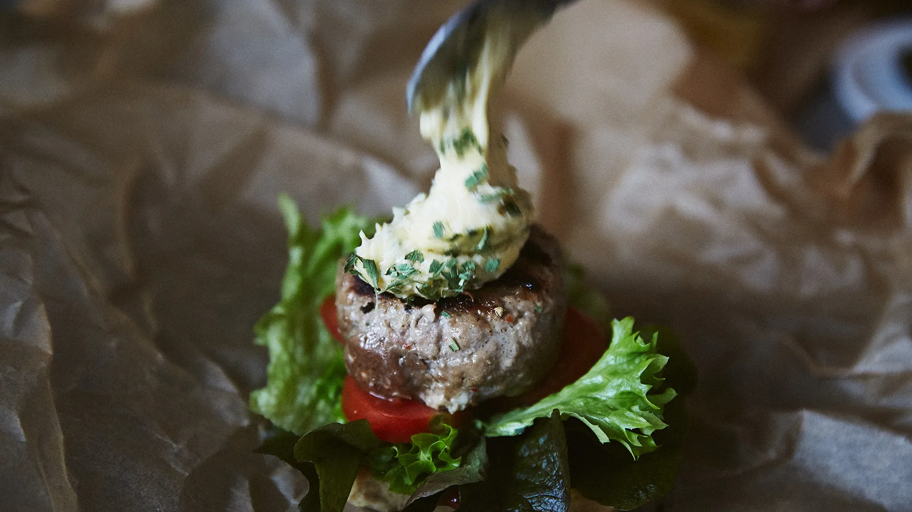Patty di manzo alla griglia con lattuga, pomodoro e topping cremoso su carta pergamena.