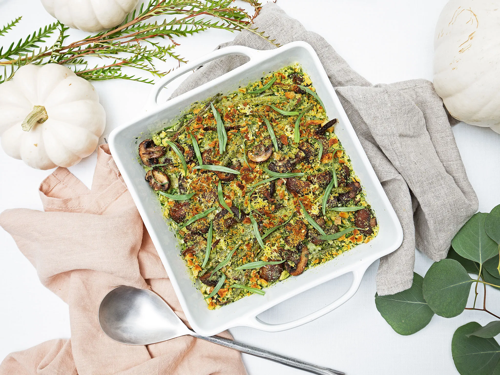 Roasted Green Beans & Mushrooms with Herbed Breadcrumbs in a white baking dish, surrounded by pumpkins and greenery.