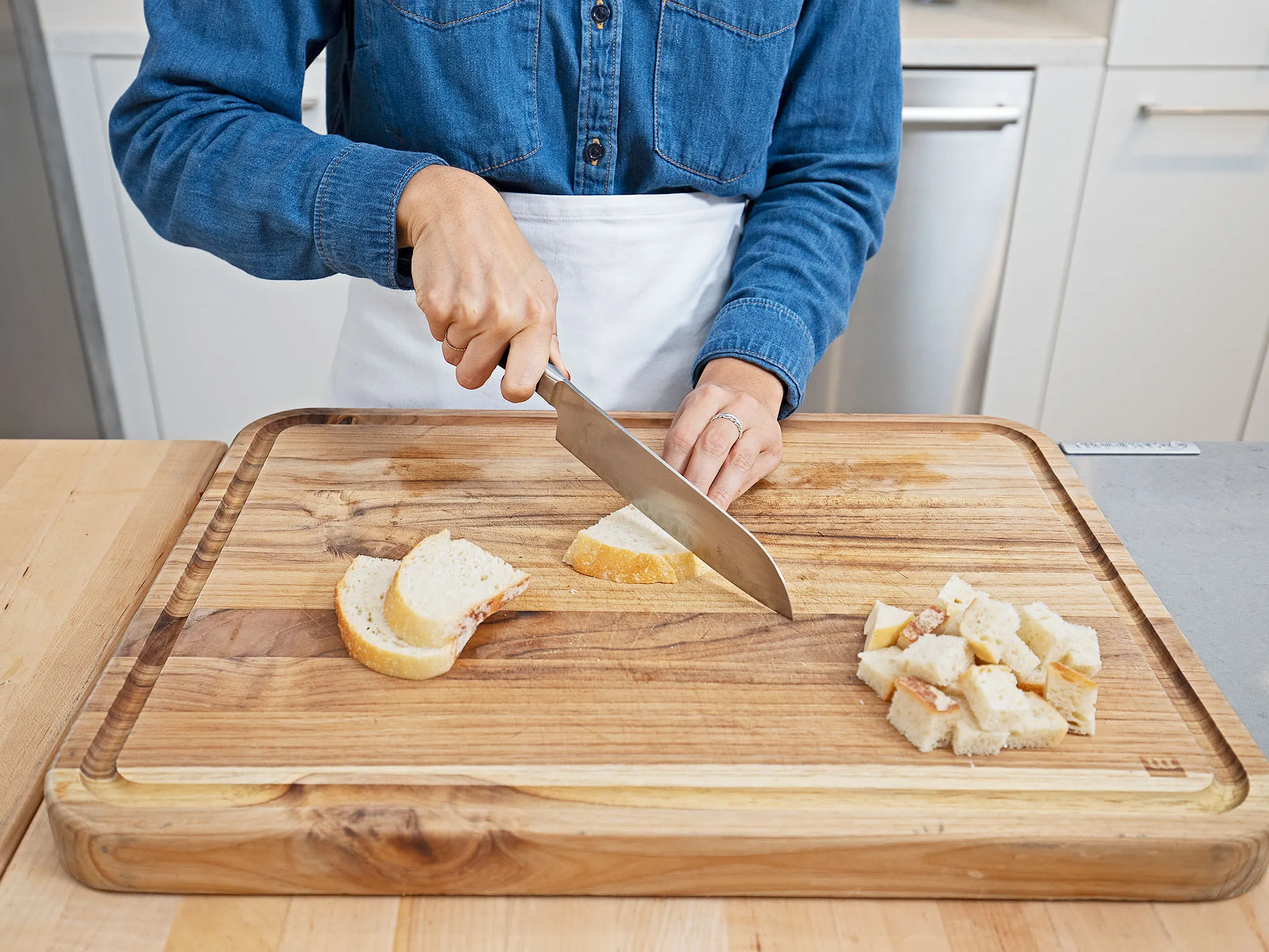 Person in denim cutting bread on a wooden board in a kitchen setting.