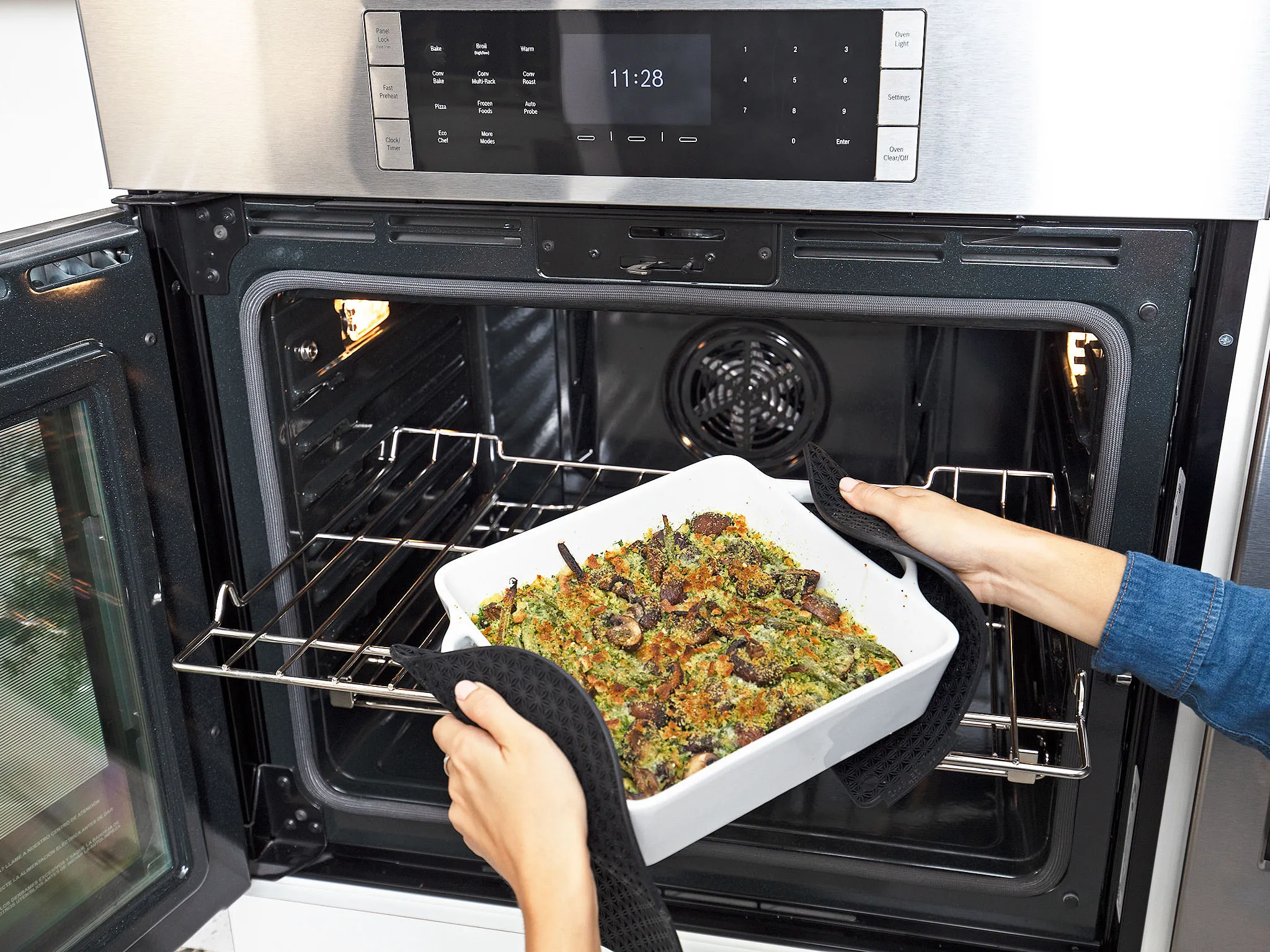Person using oven mitts to remove a casserole dish from a Bosch oven.