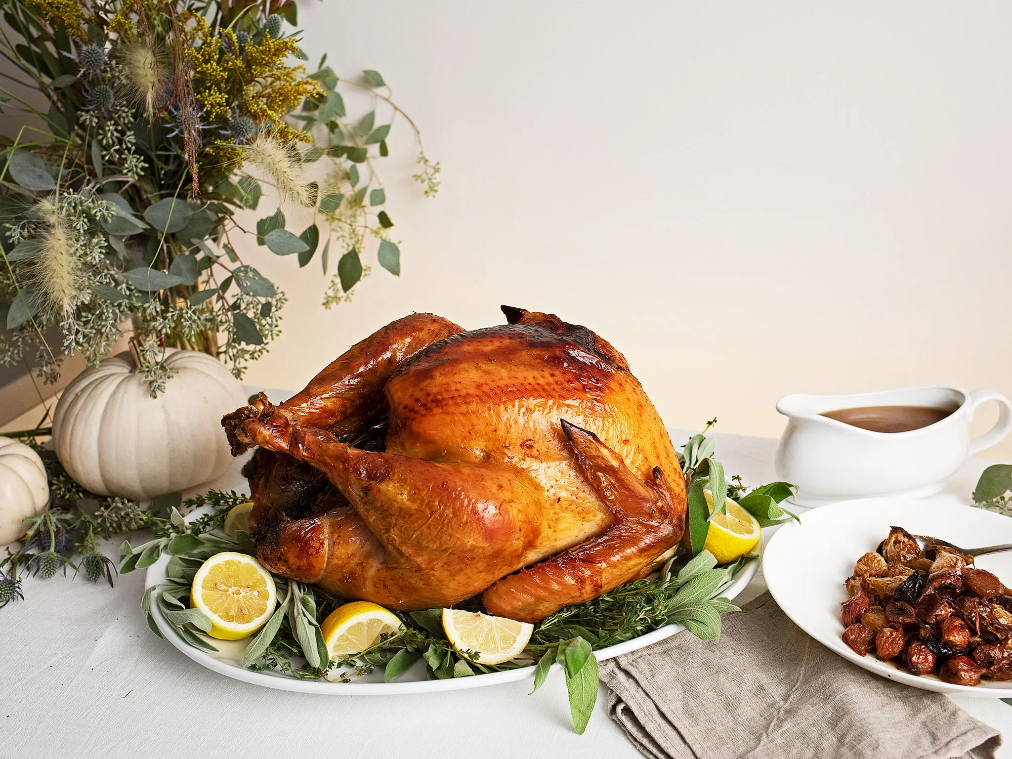 Roasted turkey surrounded by autumn foliage, pumpkins, and lemon slices on a table setting.