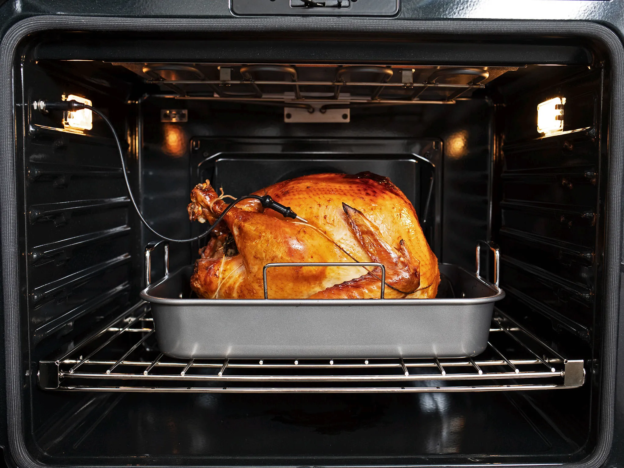 A roasted turkey with a meat thermometer in an oven tray, inside an open Bosch oven.