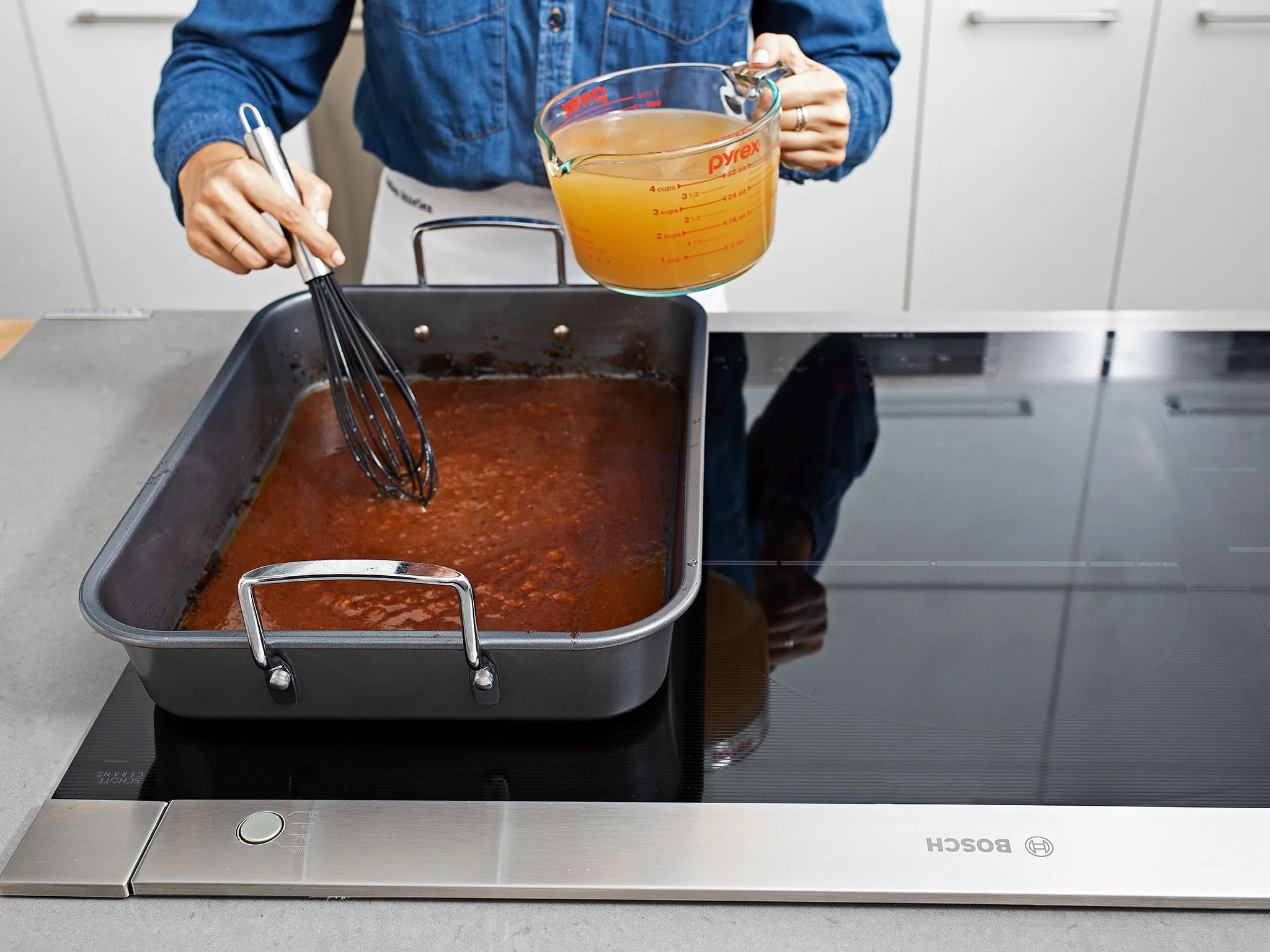 Person stirring sauce in pan on Bosch cooktop, holding measuring cup with broth.