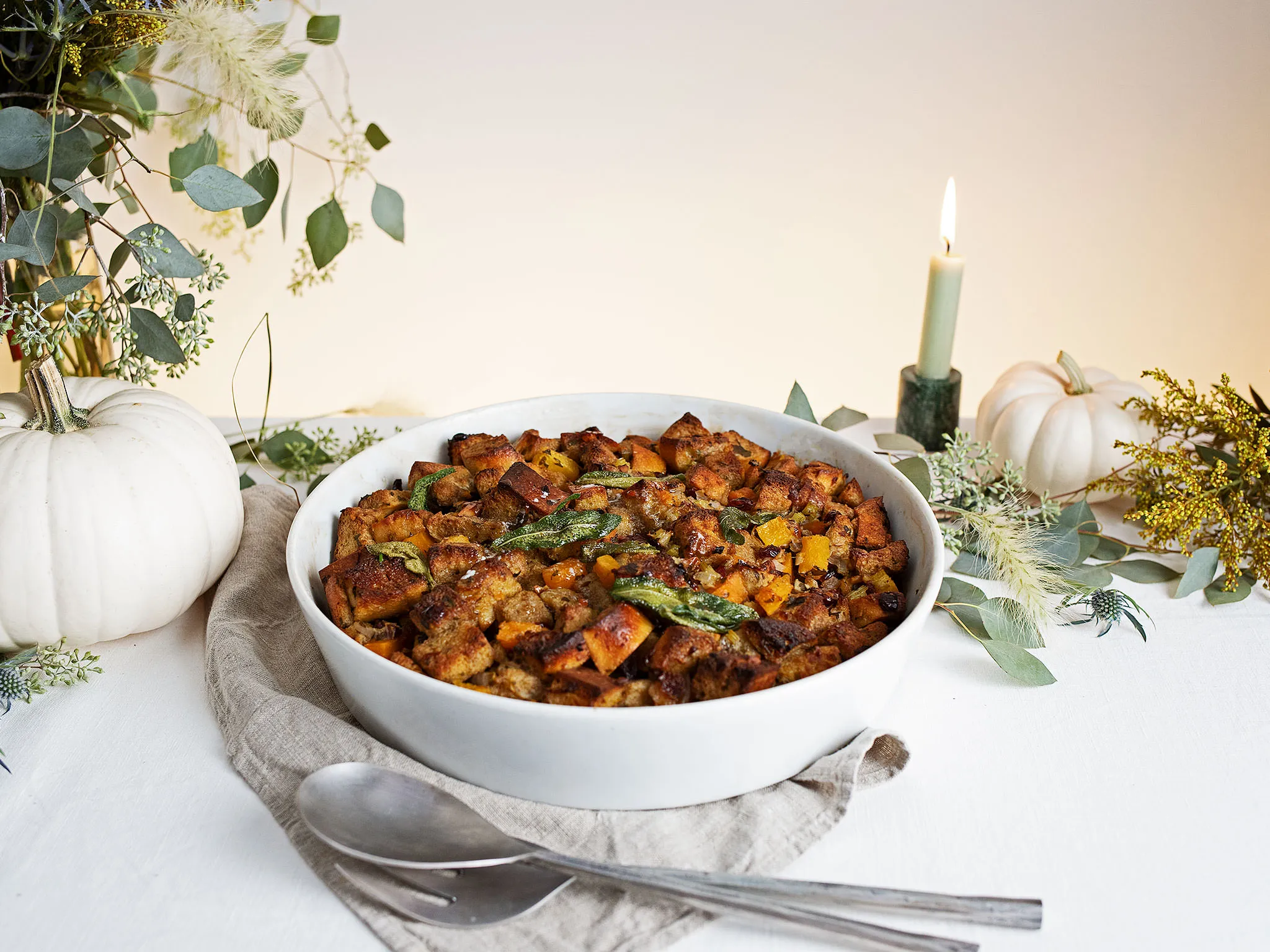 Autumn-themed dish with roasted vegetables, pumpkin, and a lit candle on a white table setting.
