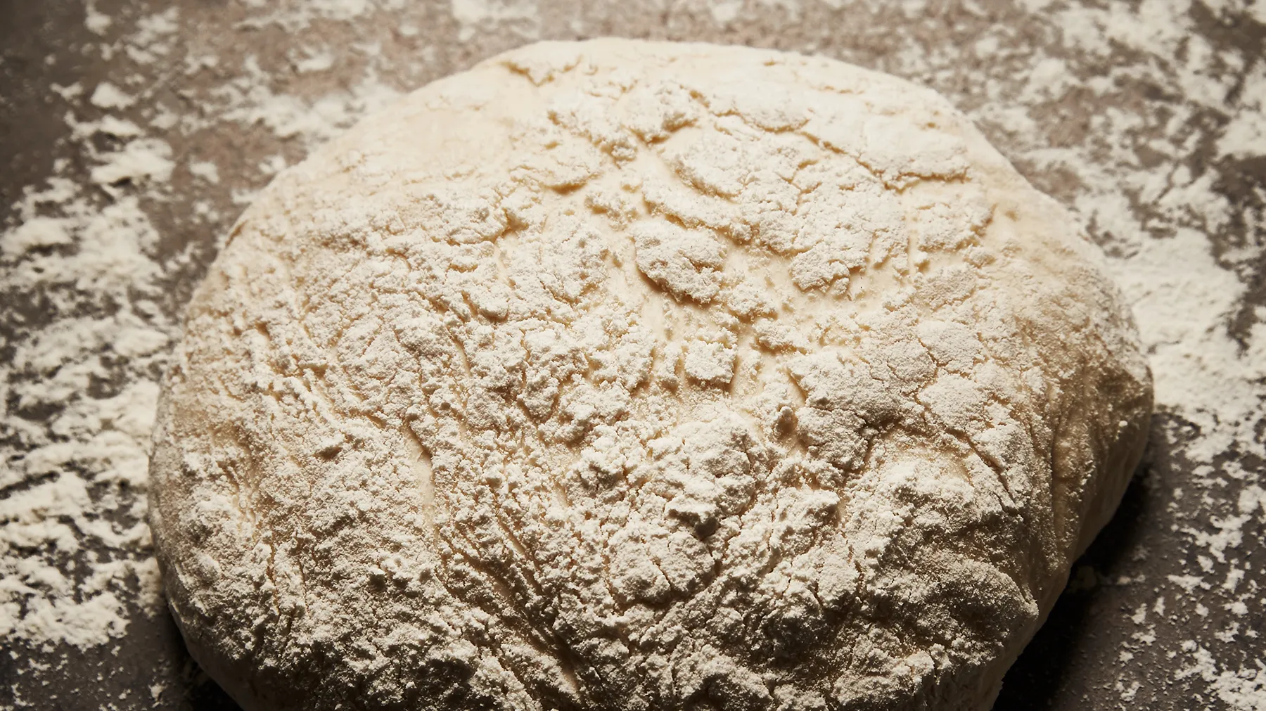 Rundes, mit Mehl bestäubtes Brot auf einer Backsteinoberfläche