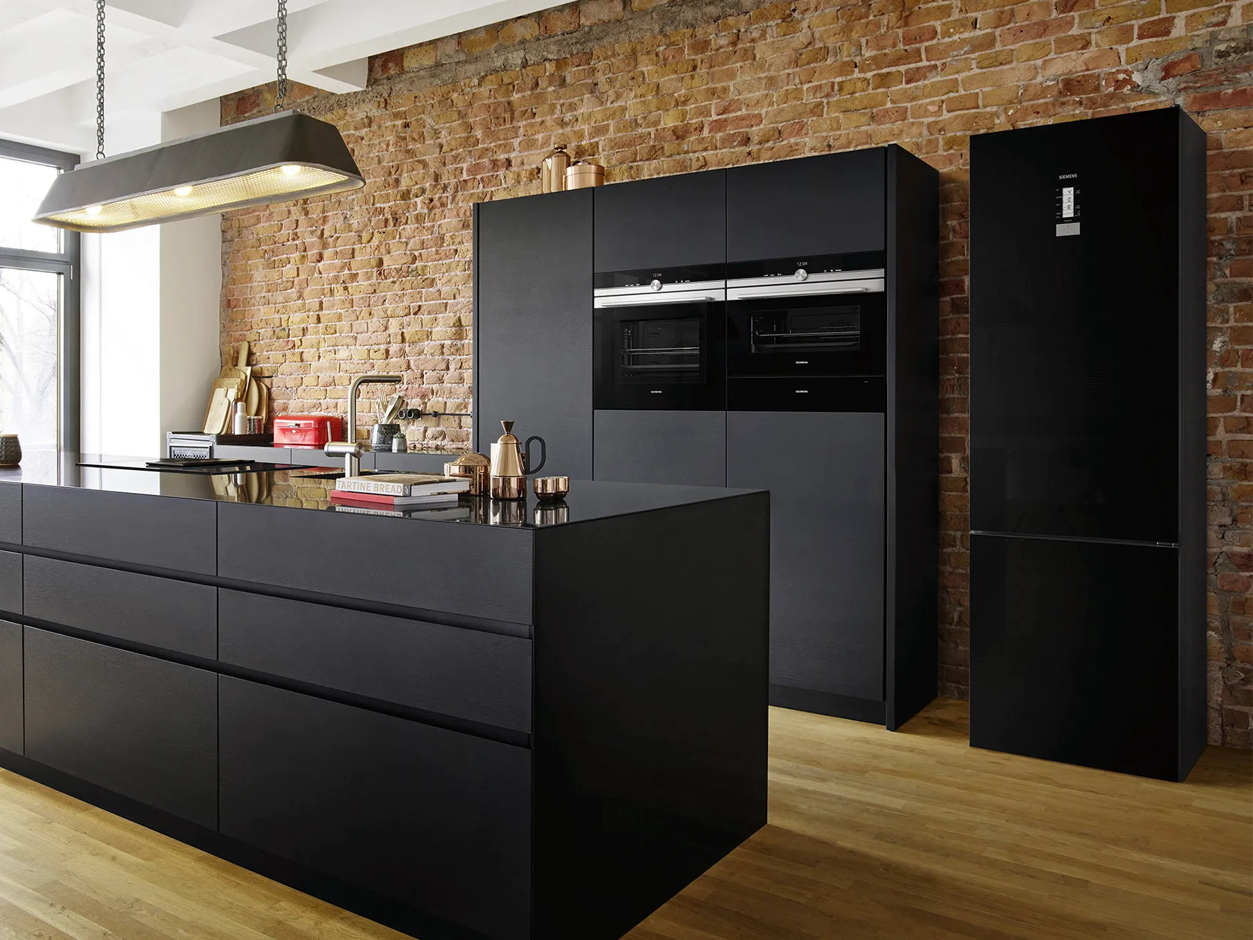 Modern kitchen with black cabinets, brick wall, and stainless steel appliances.