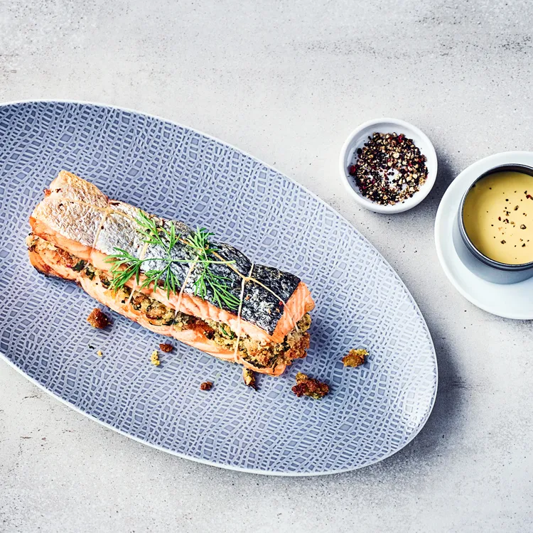 Grilled salmon fillet on a plate, garnished with herbs, served with a side of dipping sauce.