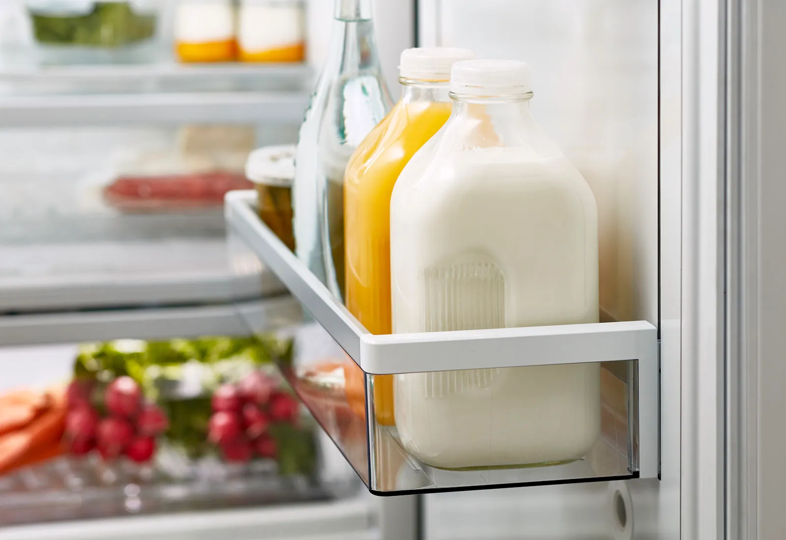 Bosch Refrigerator door shelf with bottles of milk and orange juice. Vegetables visible inside.