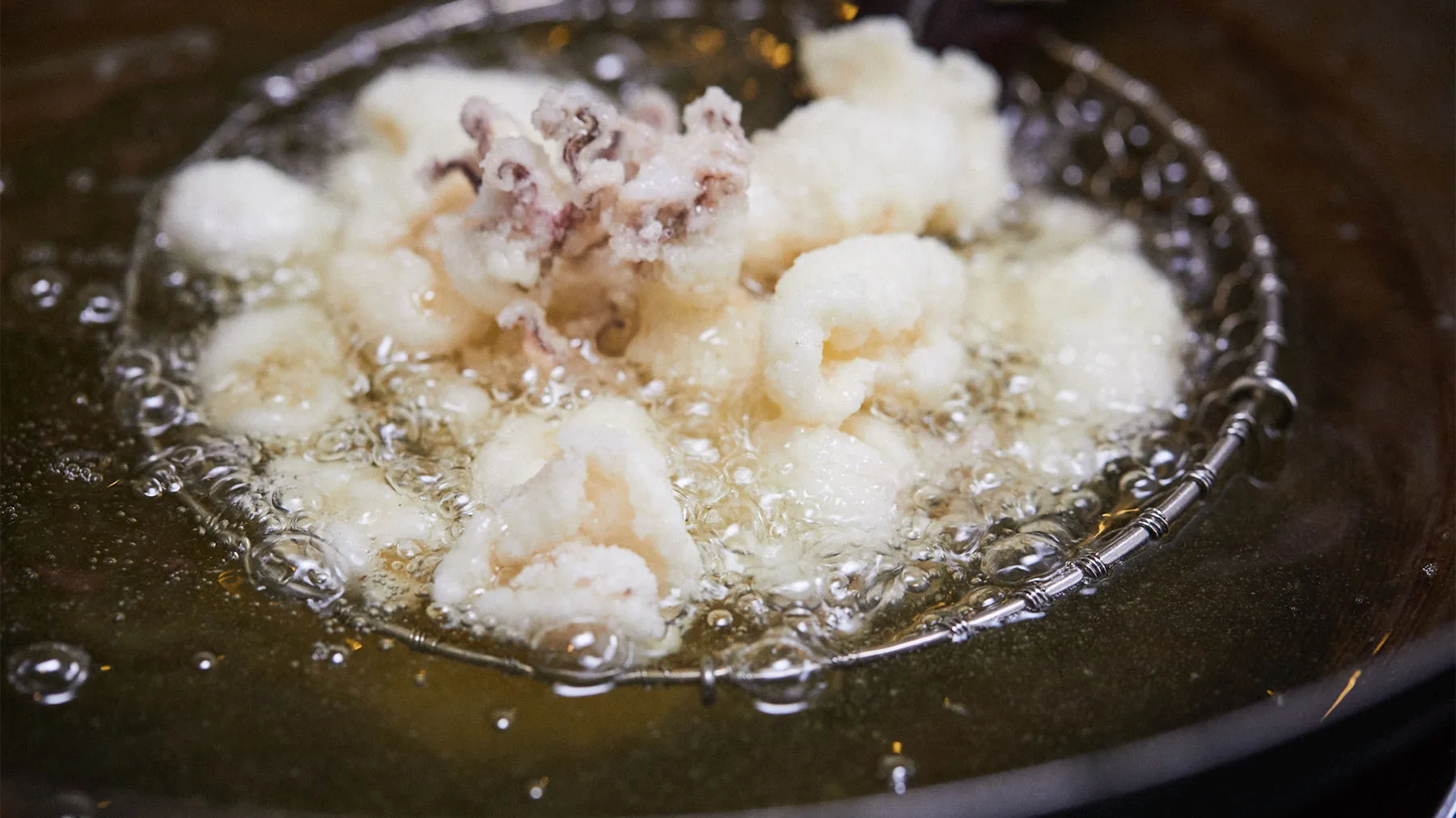 Close-up view of deep-fried, golden-brown calamari floating in hot oil, creating a bubbly, sizzling effect.