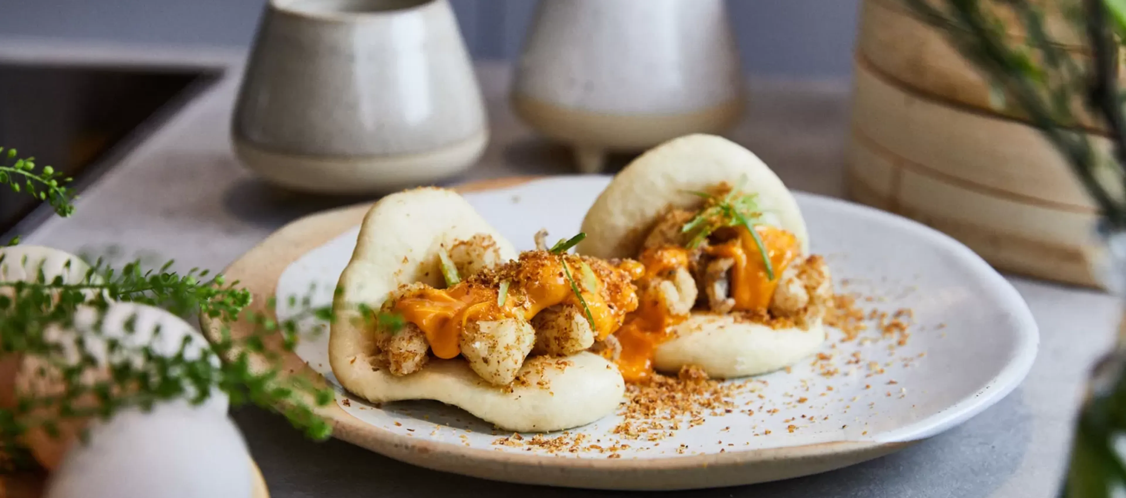 Plate with baked cauliflower, yogurt, and garnishes on wooden table with ceramic pots.