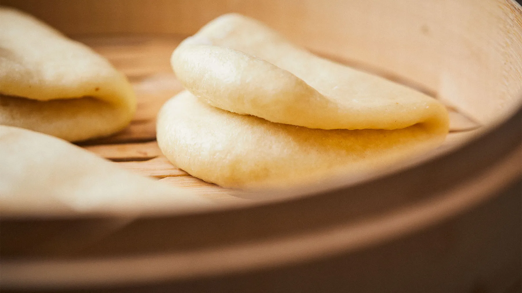 Freshly baked bao on a wooden plate, golden-brown in color and fluffy in texture.