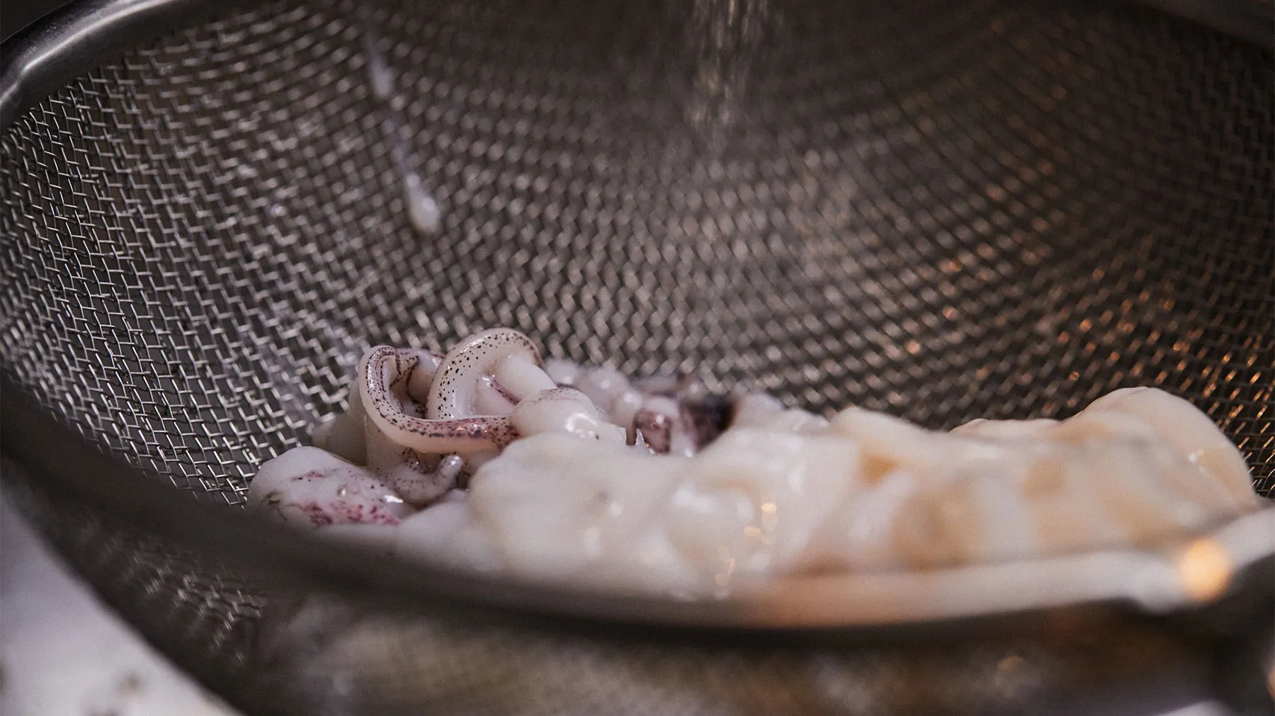 Shrimp being cooked in a metal mesh basket, with steam rising from the cooking surface.