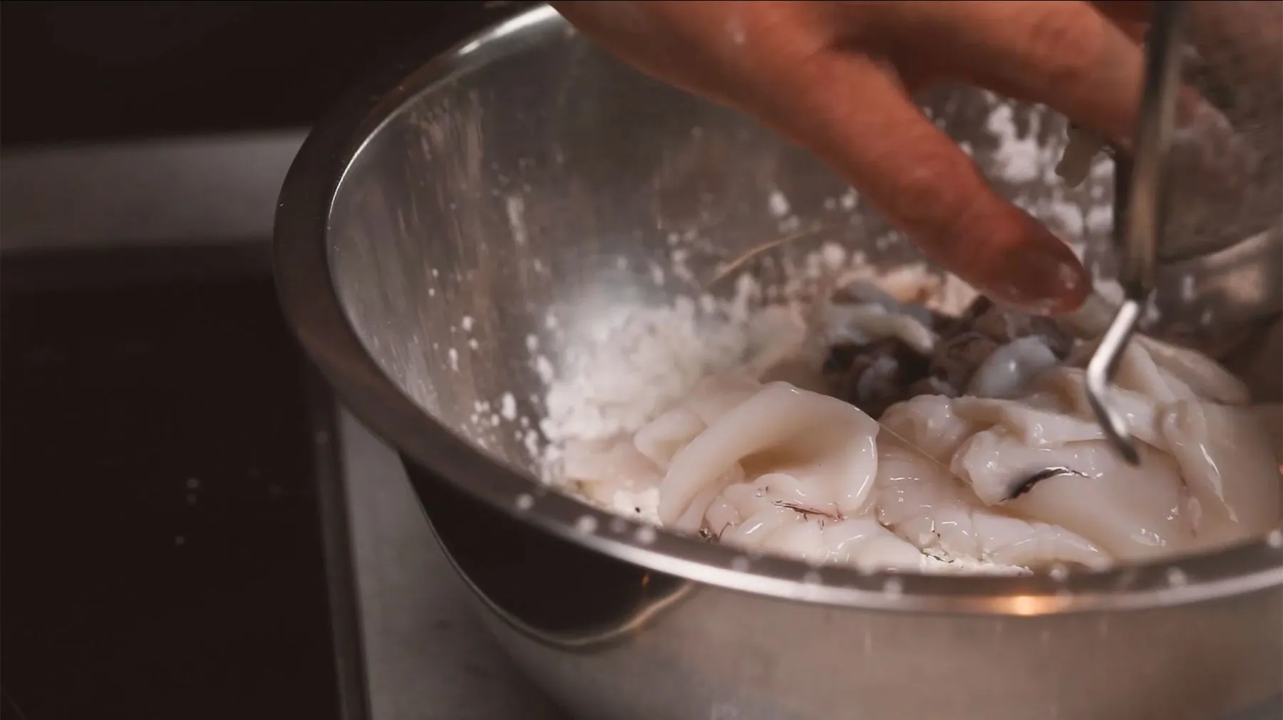 Hands stirring a pot of boiling water with mushrooms or other ingredients.