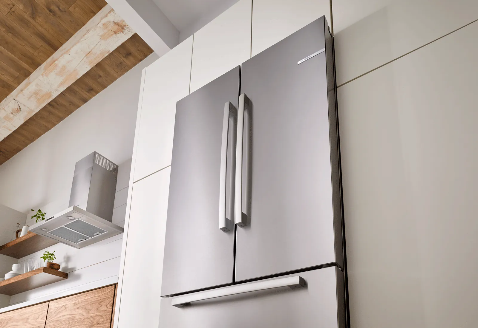Modern kitchen with Bosch stainless steel refrigerator, wooden shelves, and white cabinets.