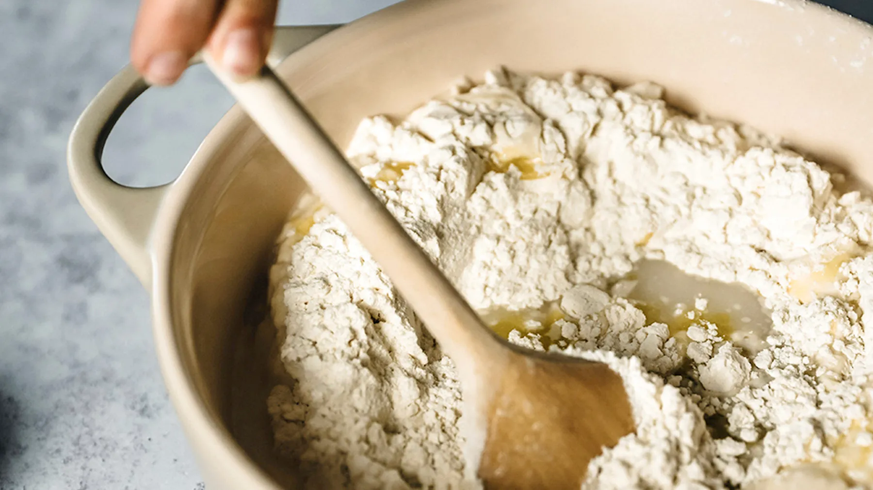 Hand rührt mit Holzlöffel in Schüssel mit Mehl und etwas Öl