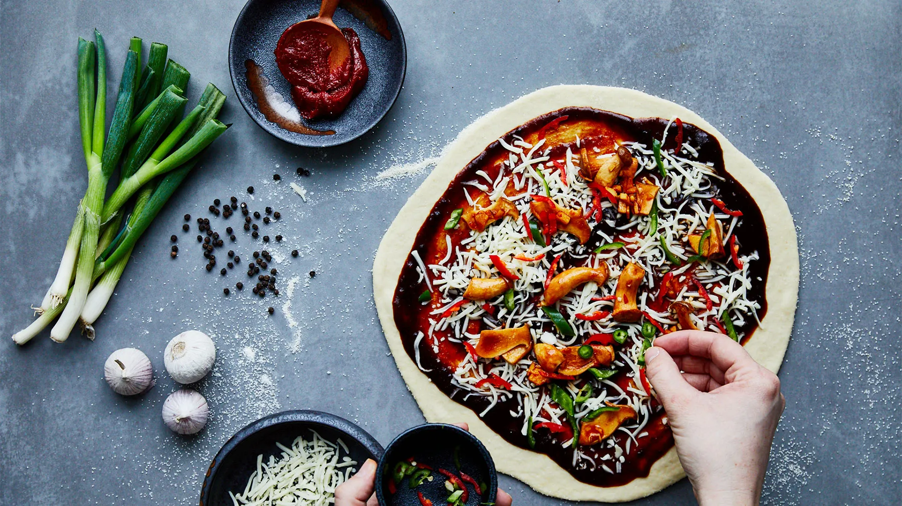 Pizzateig mit Tomatensauce, Käse und verschiedenen Toppings, die auf einem Küchentisch zubereitet werden.