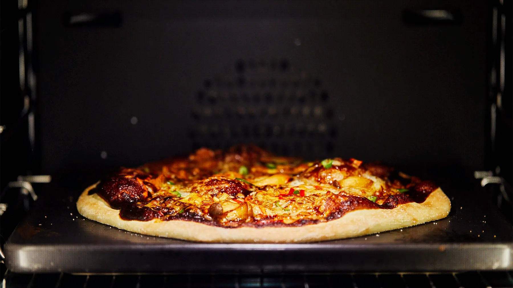 Frisch gebackene Pizza mit geschmolzenem Käse, Paprika und anderen Toppings in einem dunklen Ofen.