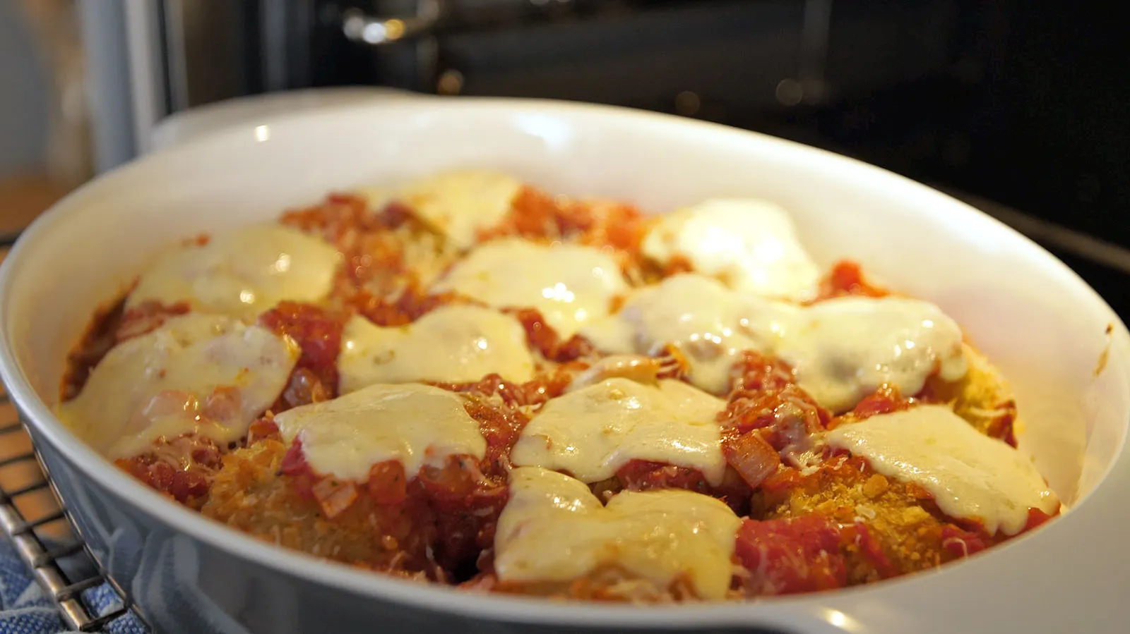 A white oval baking dish filled with golden-brown, cheese-covered rice balls in a rich tomato sauce, fresh out of the oven.