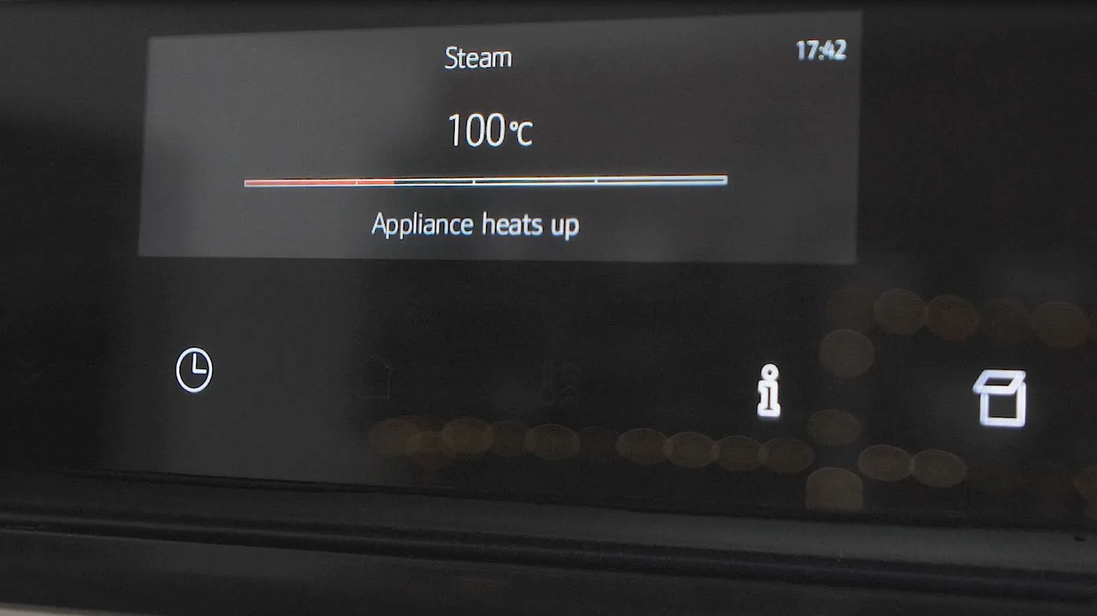 A close-up of a Neff oven's digital display showing "Steam" function set to 100°C, with a progress bar indicating the appliance is heating up.