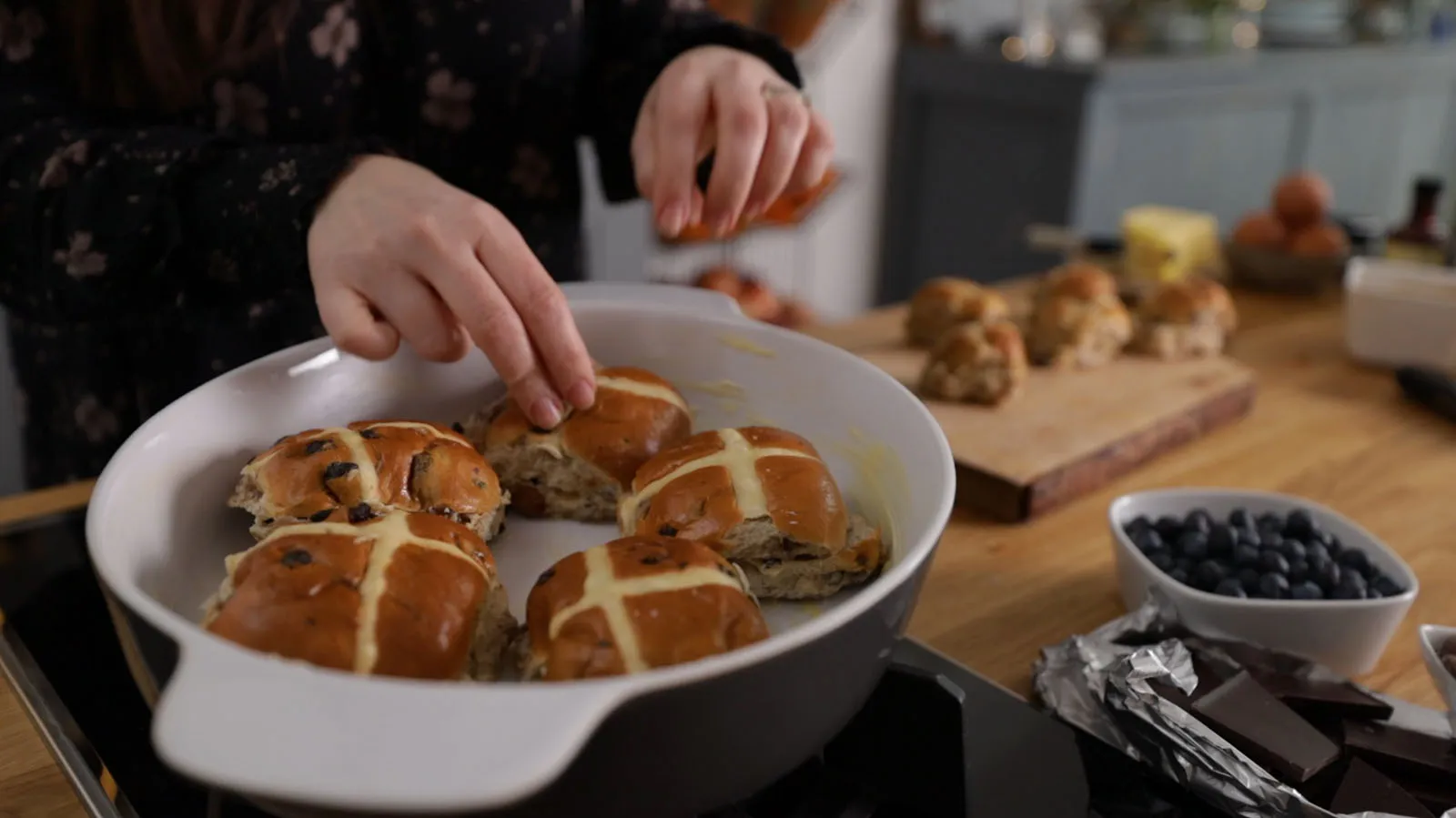 Person arranging hot cross buns in baking dish