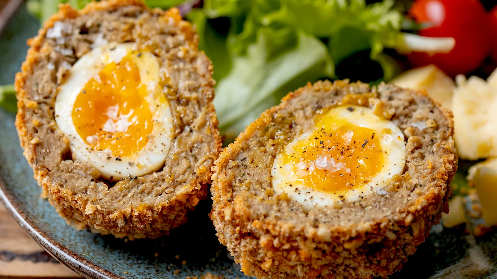 Scotch egg cut in half on plate with salad