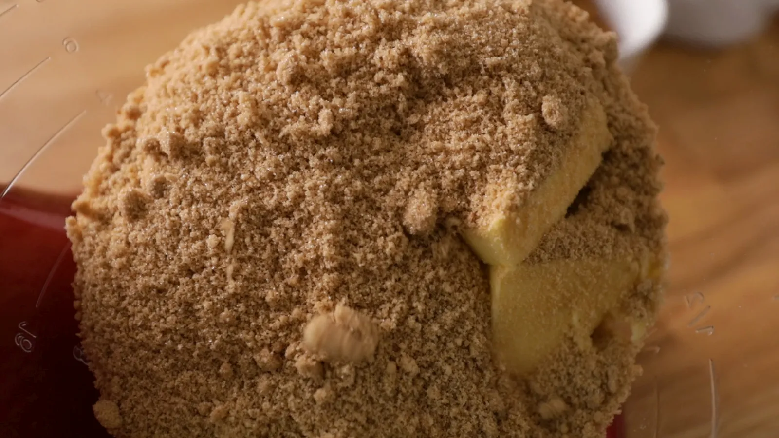 A close-up of a food processor bowl filled with brown sugar and cubes of butter.