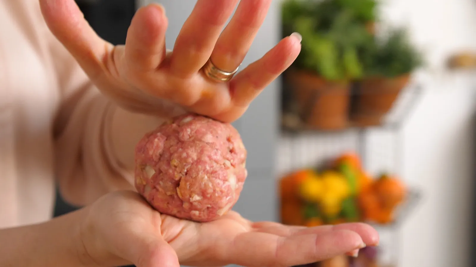 Hands shape a raw burger patty into a perfect round ball.