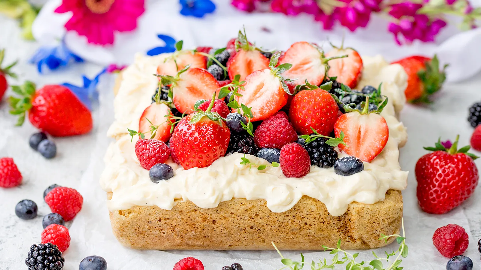 Iced cake topped with berries with various berries next to it
