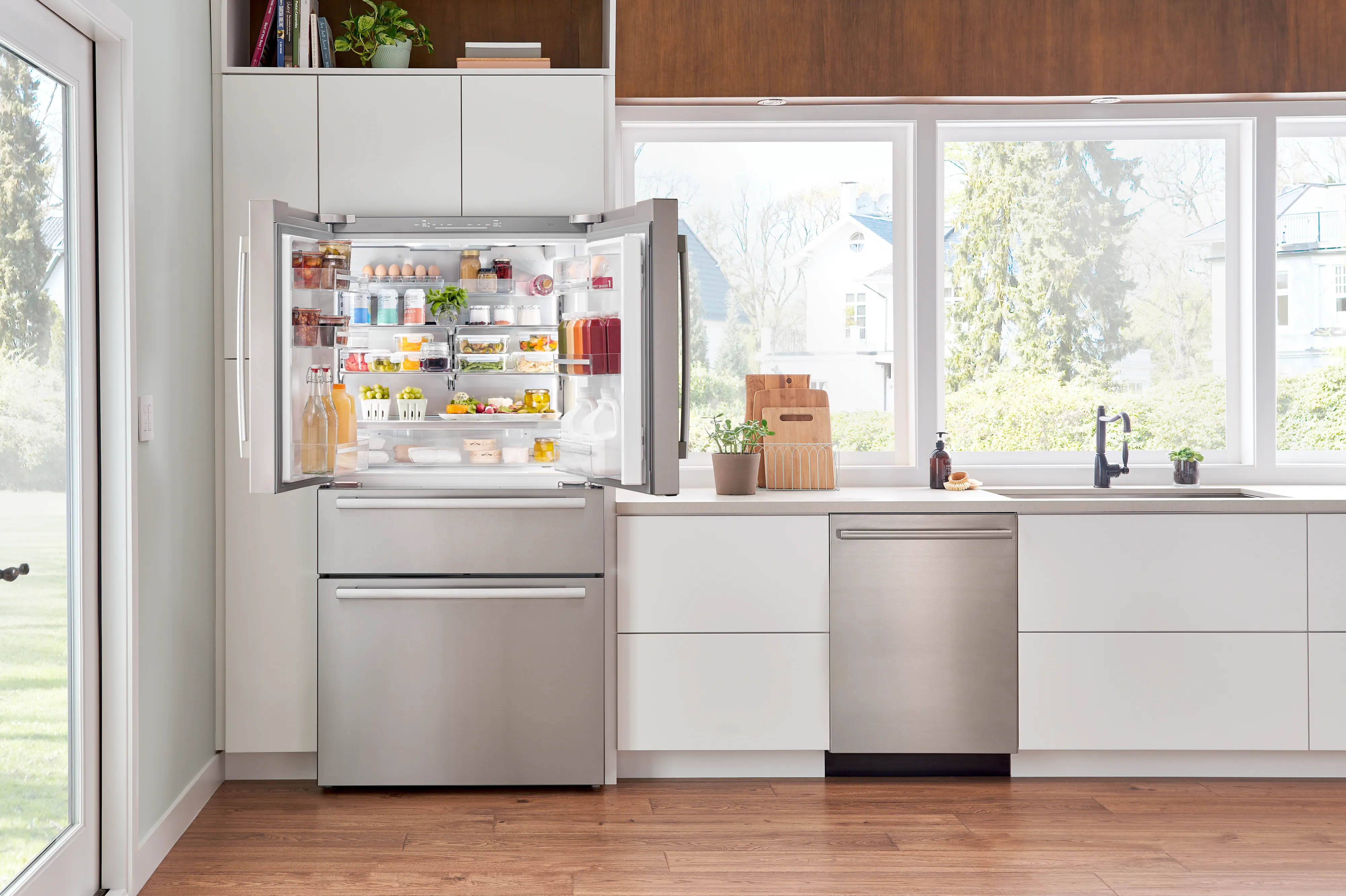 A modern kitchen features a stainless steel fridge with open doors, showcasing organized shelves filled with food and beverages.