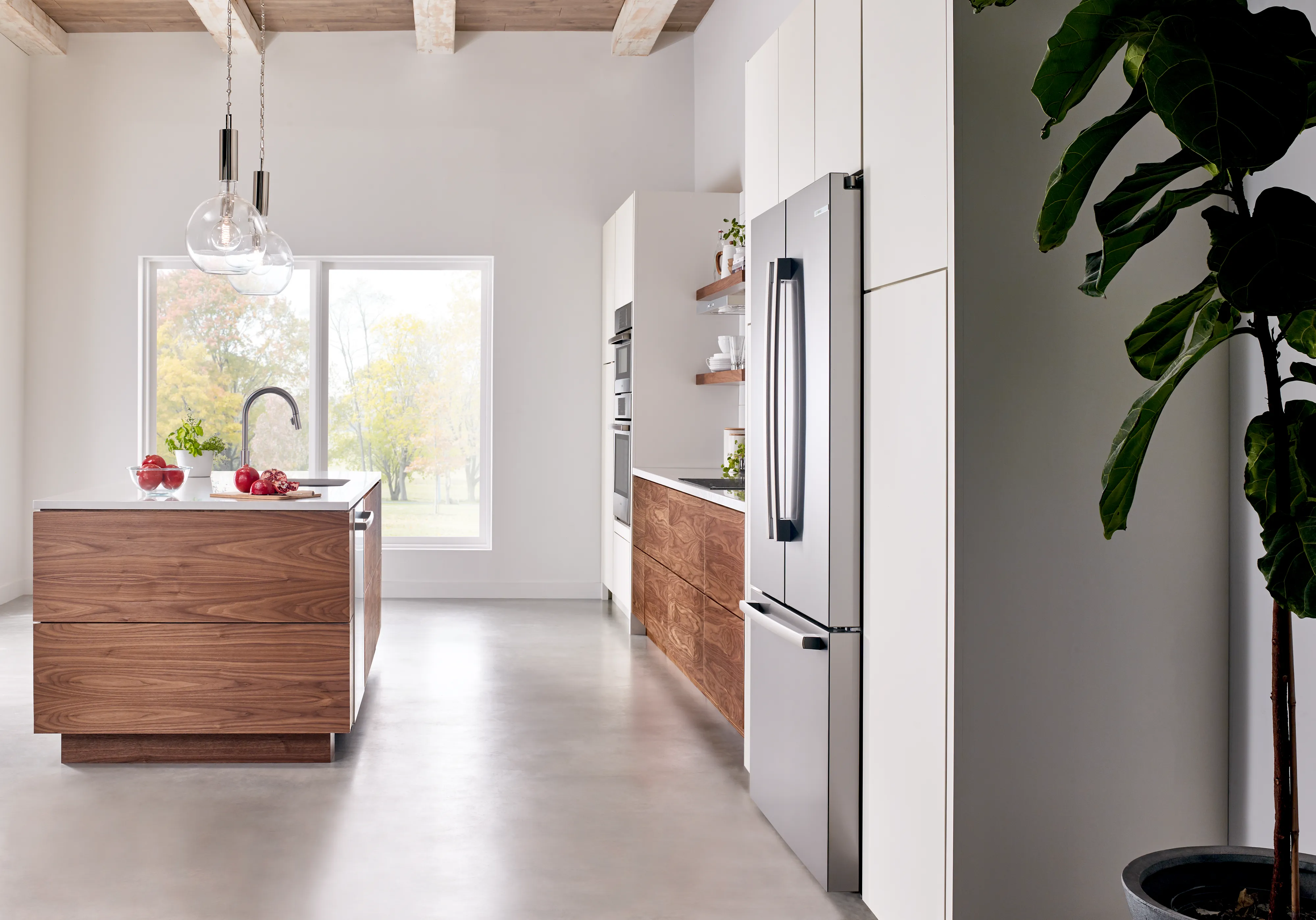 Modern kitchen with a Bosch Compact stainless steel fridge, wooden island, plants, and ample natural light.