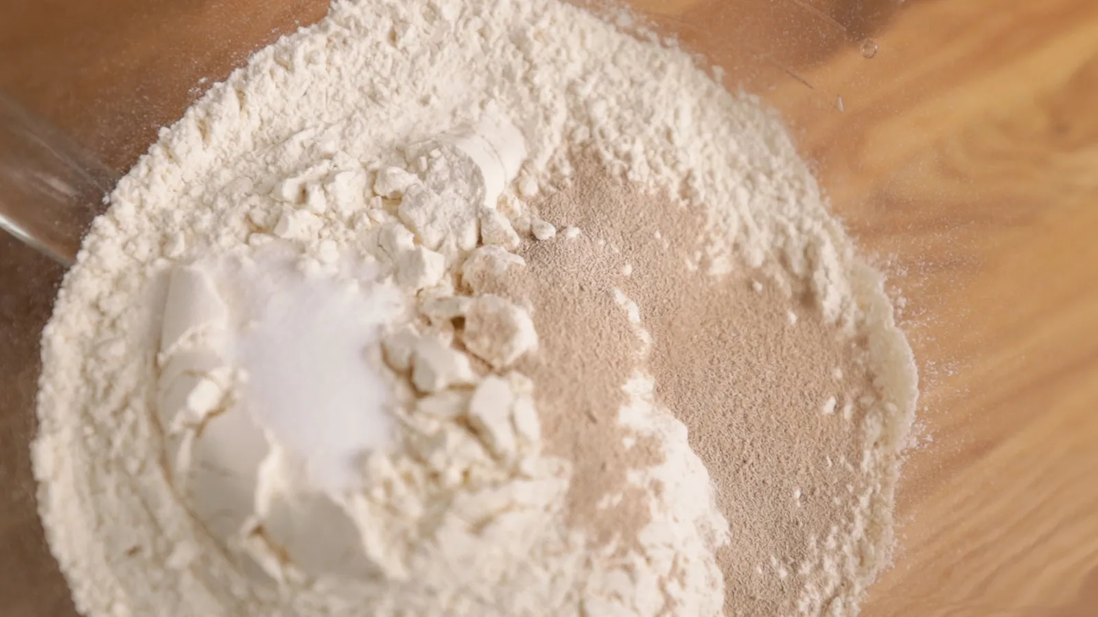 Pile of white powdery substance, possibly flour or baking ingredient, on a wooden surface.