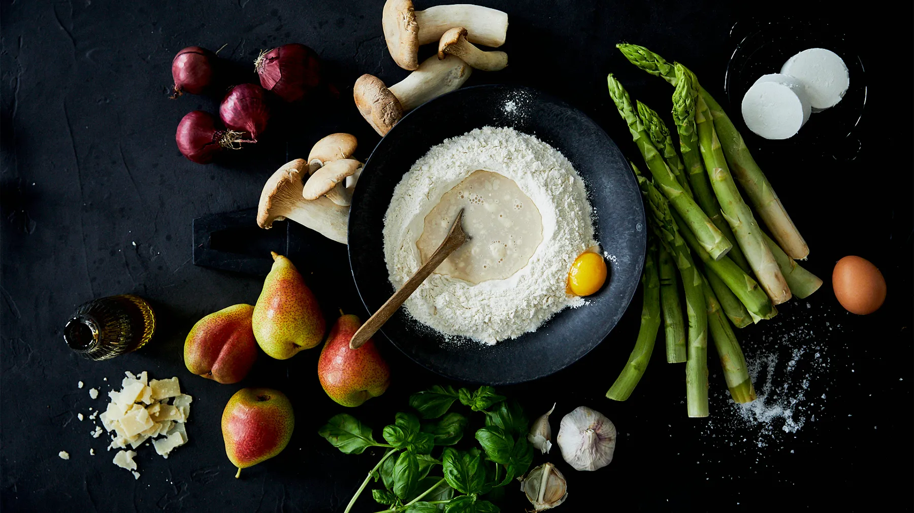 Assorted fresh produce, baking ingredients, and cooking utensils arranged on a dark background.