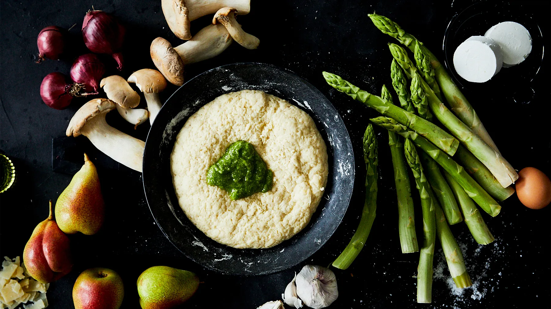Assortment of fresh produce, including asparagus, pears, radishes, and a bowl of creamy dip or spread.