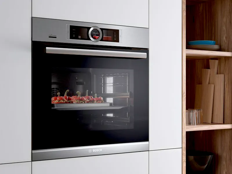Modern kitchen oven with fresh produce inside, surrounded by wooden shelves.