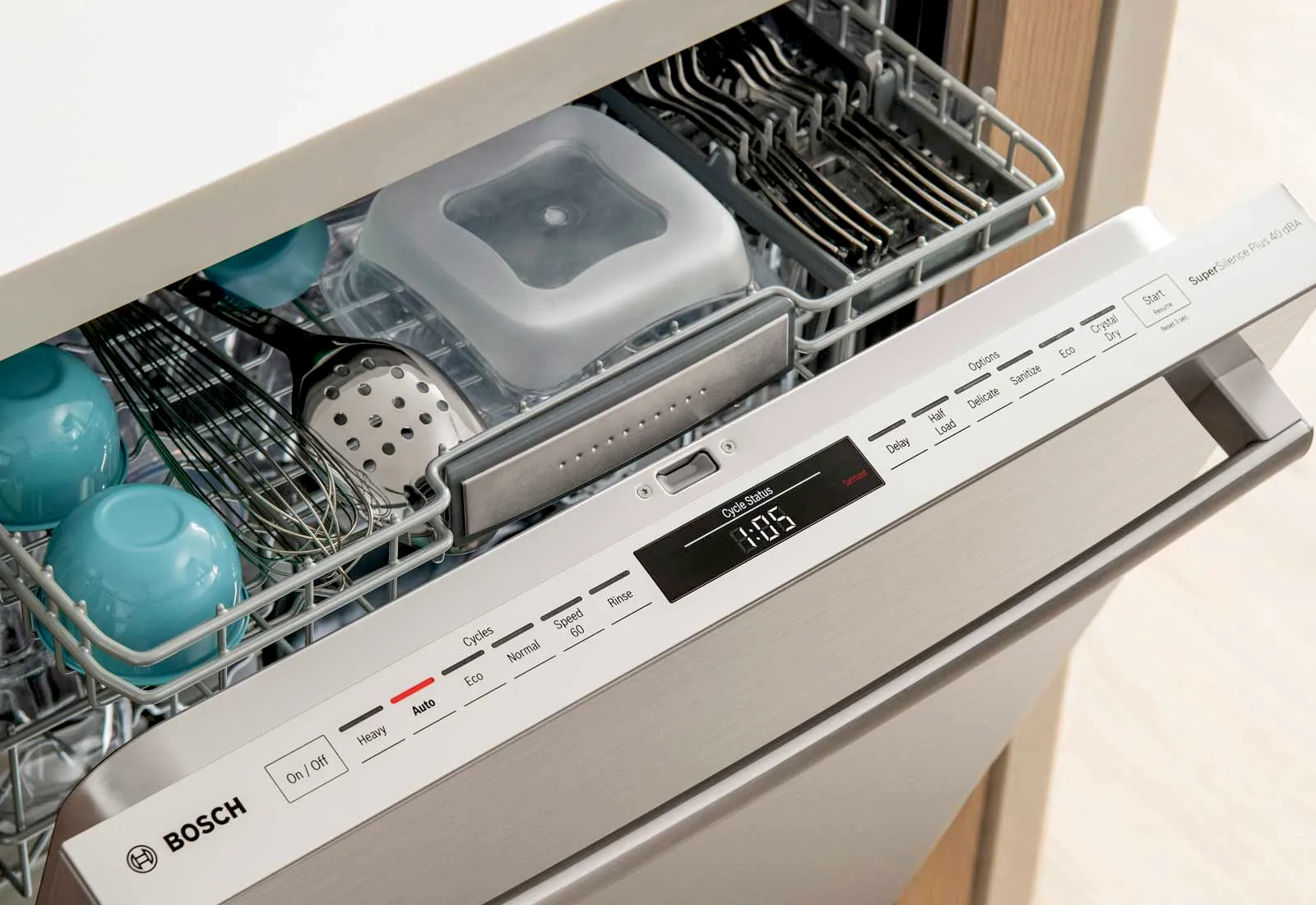 Bosch dishwasher interior with utensils and cups loaded on the top rack, panel displays settings.
