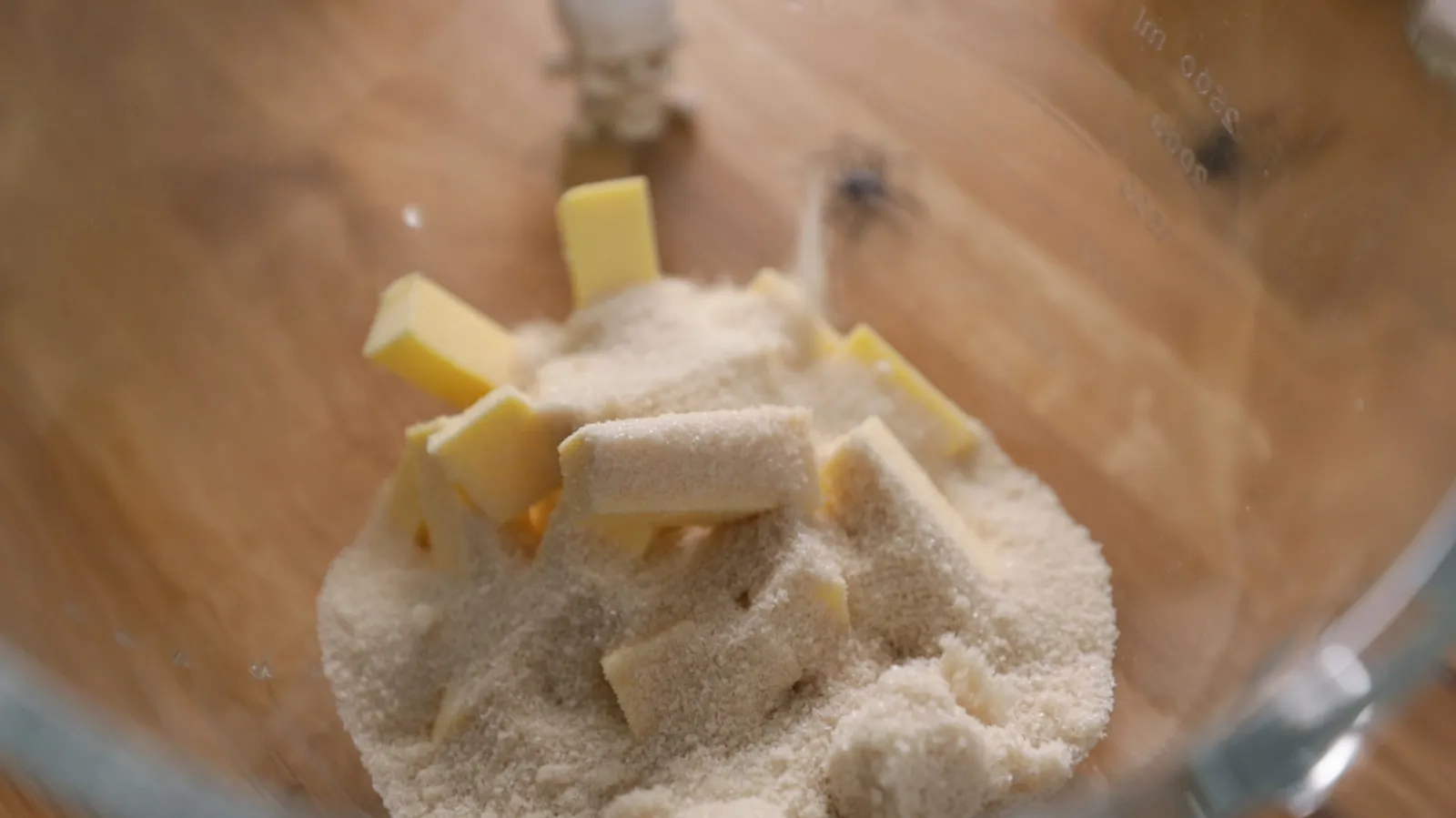 A close-up of a blender filled with white powder (likely flour or sugar) and cubes of butter.