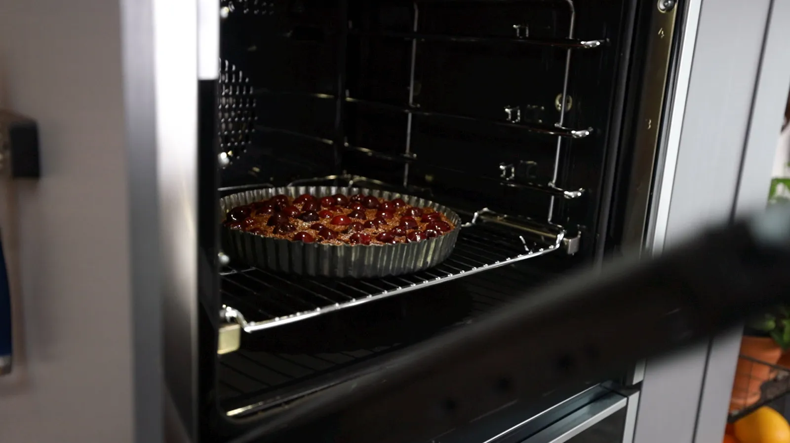 A fluted tart pan filled with a chocolate and cherry tart is placed into a hot oven.