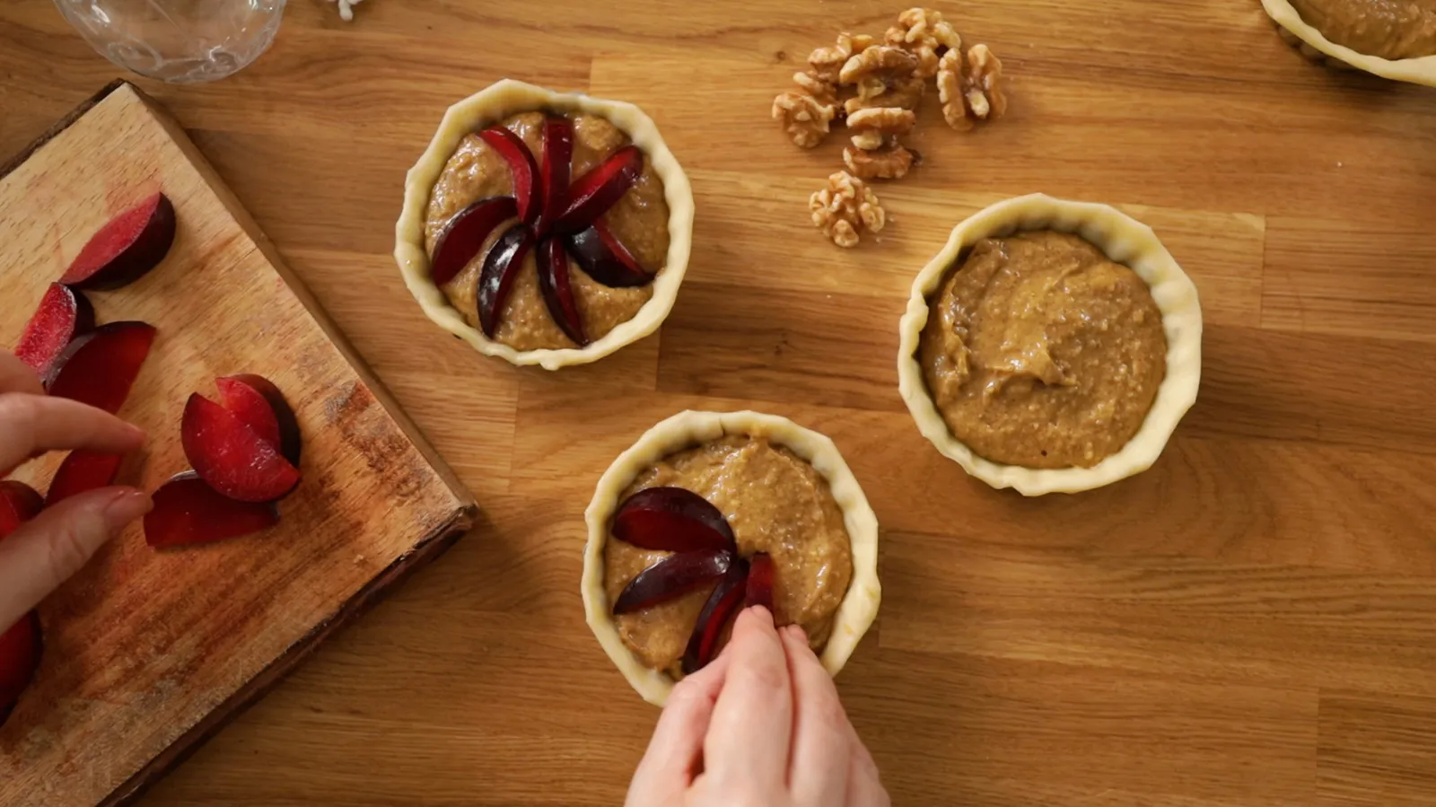 Sliced plums being added to top of tarts