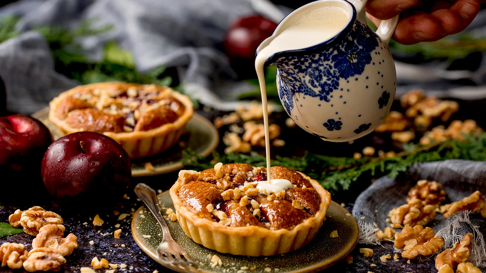 Cooked tart on plate with festively decorated background, cream being poured on top