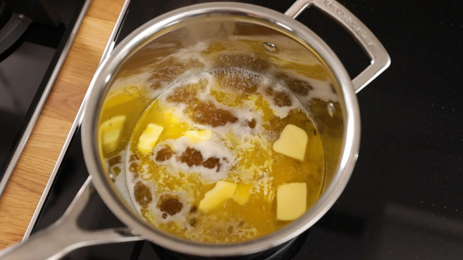 An overhead view of a stainless steel saucepan on an induction cooktop, containing melted butter and water, bubbling gently.