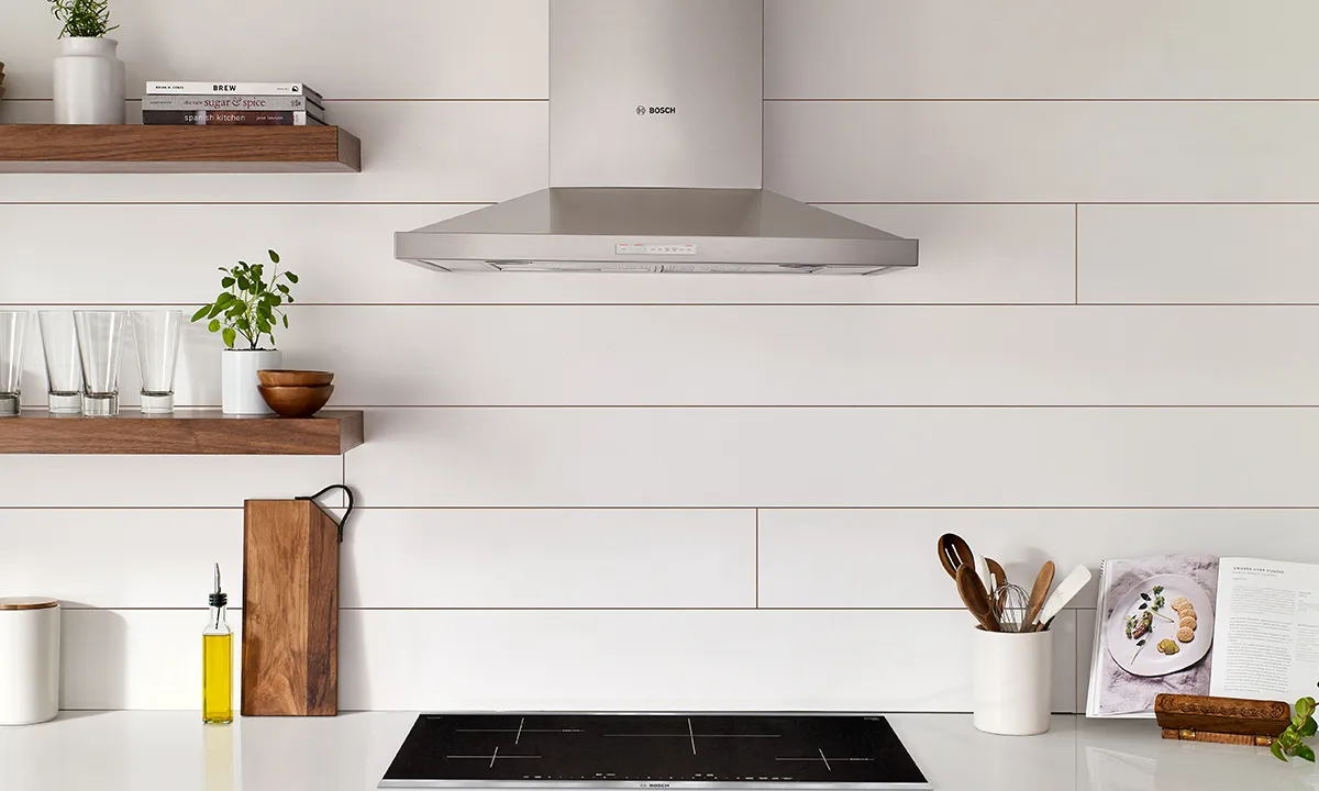 Modern kitchen with Bosch range hood, Bosch induction cooktop, wooden shelves, and kitchen accessories.