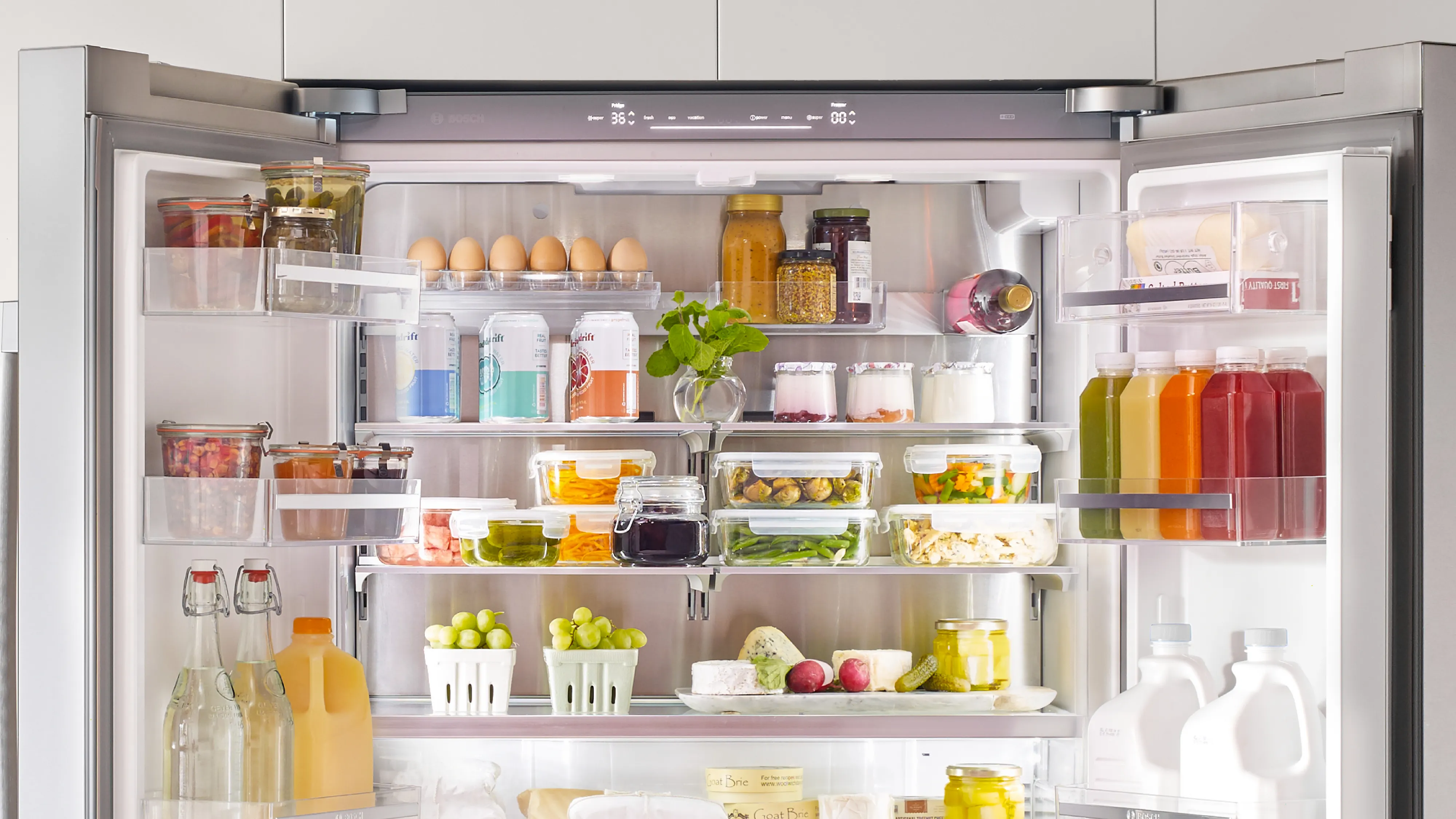 Open Bosch refrigerator filled with various food items, including fruits, vegetables, condiments, and beverages.