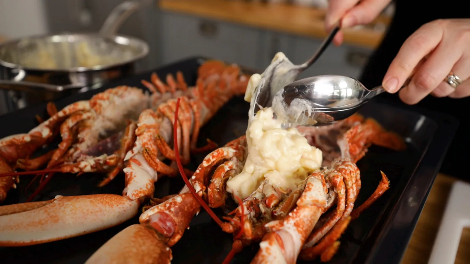 Cooked lobster tails and claws on a plate, with a hand using a utensil to serve the dish.