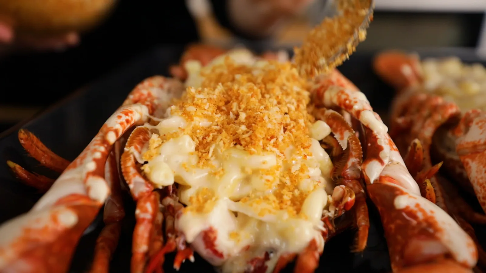Cooked lobster tail with melted cheese and breadcrumb topping, close-up view.