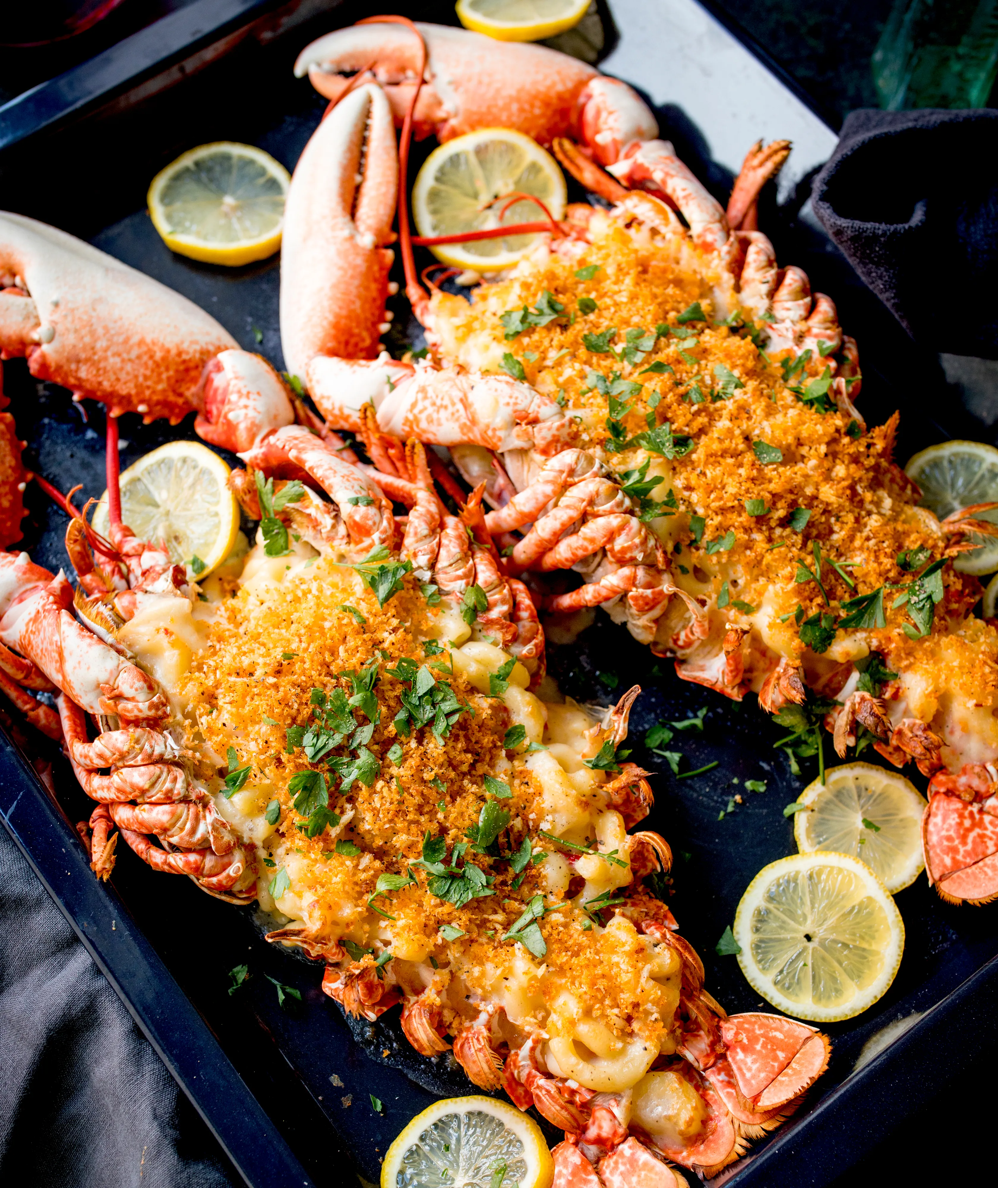 Cooked lobsters with lemon slices, garnished with parsley on a dark background.