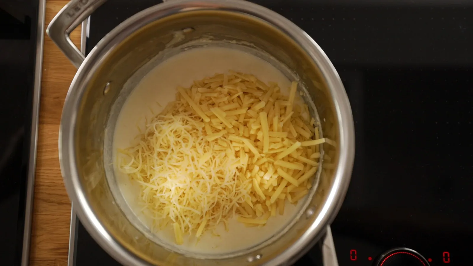 Pot of boiling water with shredded cheese, cooking pasta on stove.