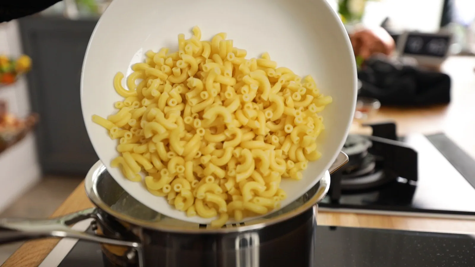 Cooked macaroni pasta in a white bowl on a stove top.